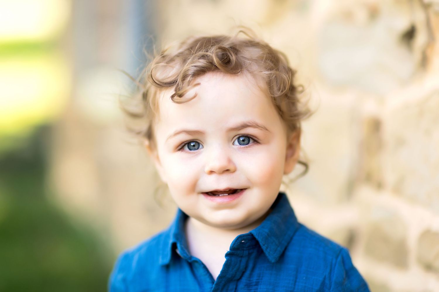 Young child in blue shirt smiling warmly at the camera.