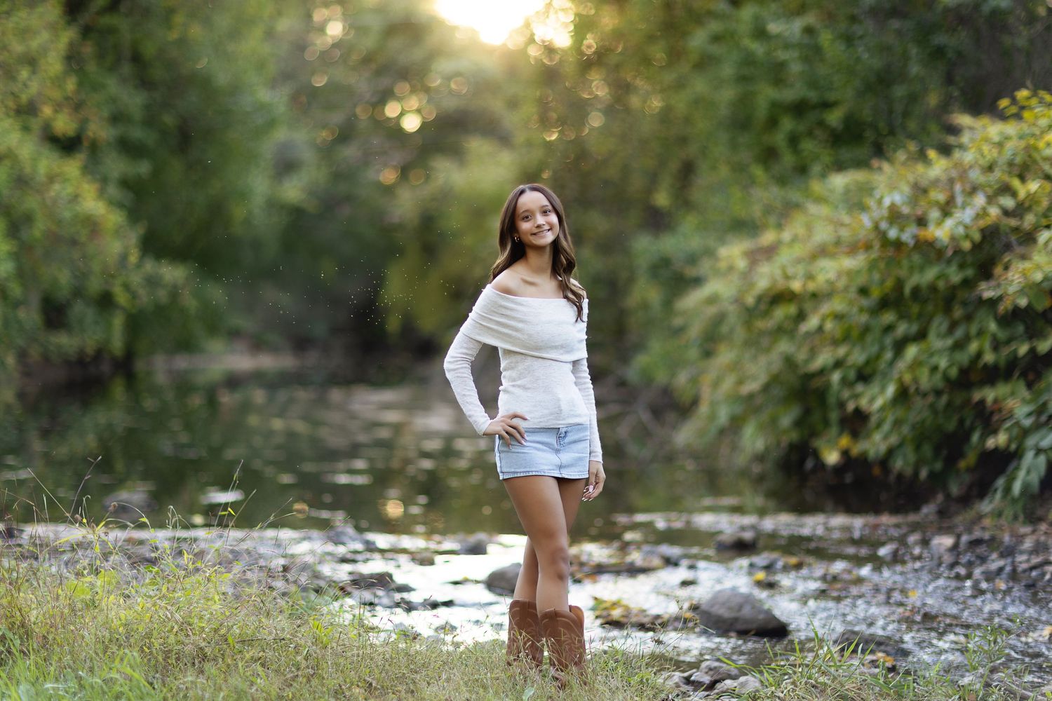 Woman in casual attire sits by rocky stream during outdoor photo session.