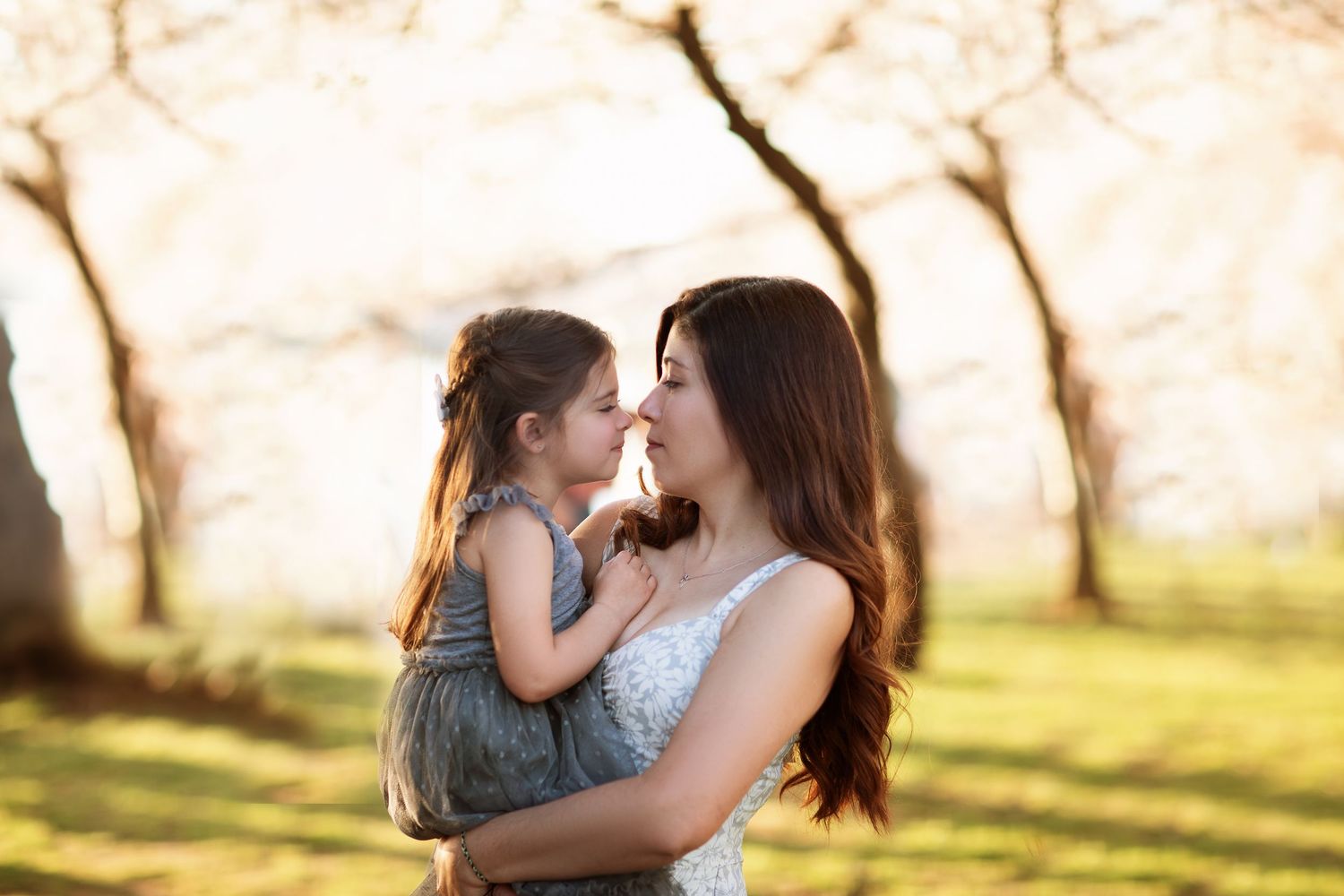 A tender moment between parent and child in a sunlit spring orchard with blooming trees in the background.