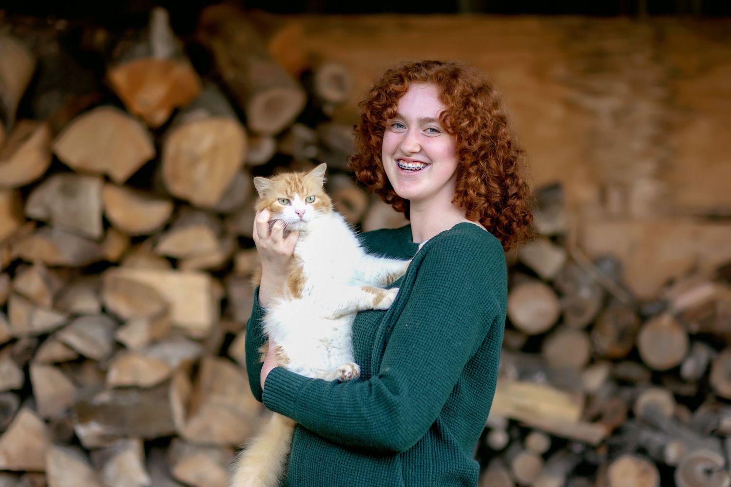 White cat being held against rustic wood pile background.