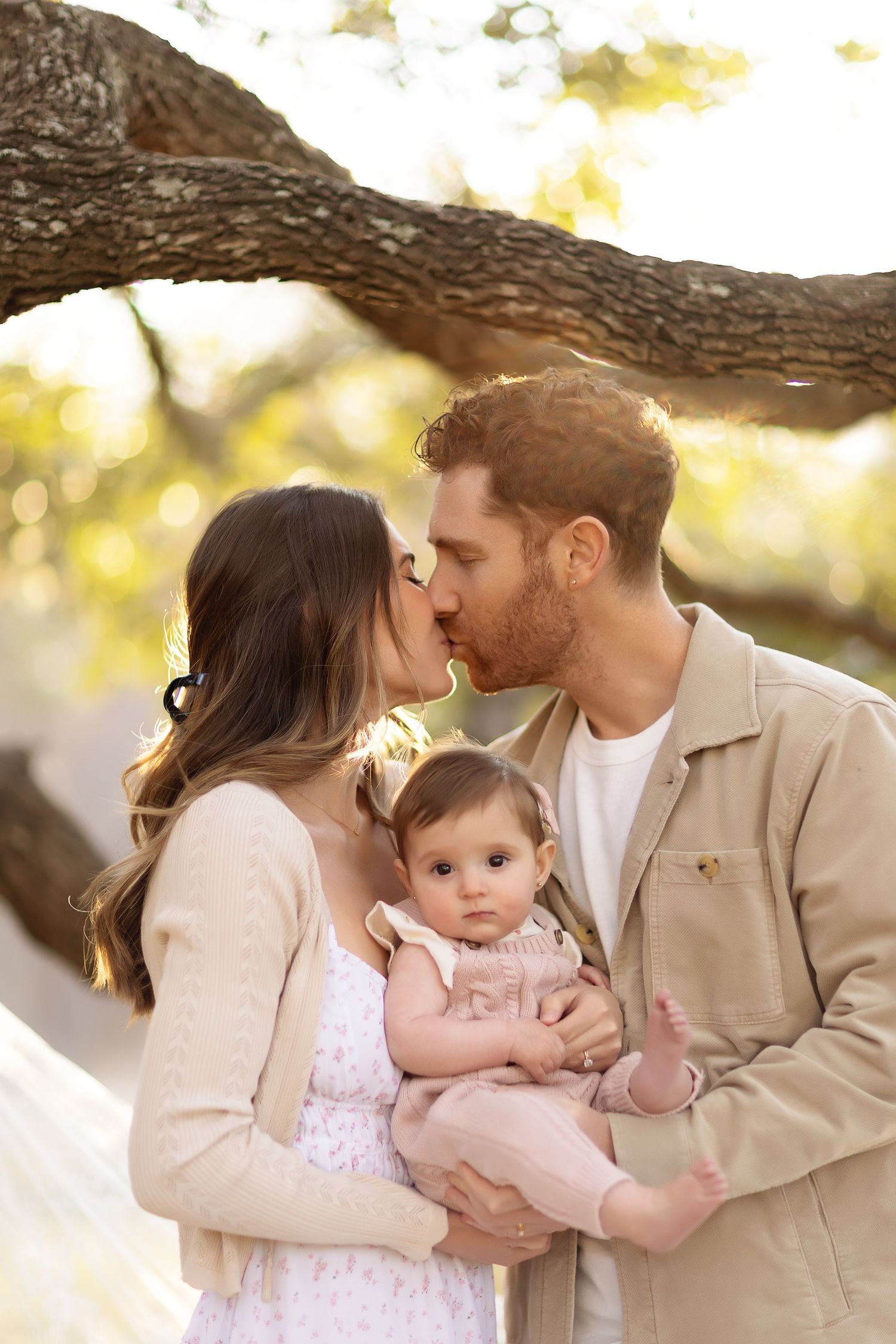 A loving family shares tender moments together under a tree branch during a golden sunset photoshoot.
