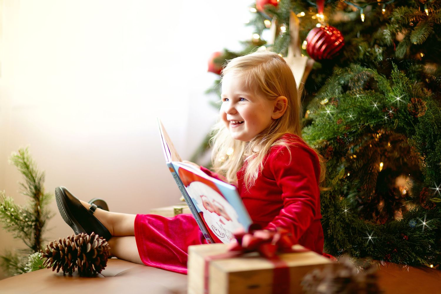 Child in red pajamas enjoying Christmas morning activities near decorated tree.