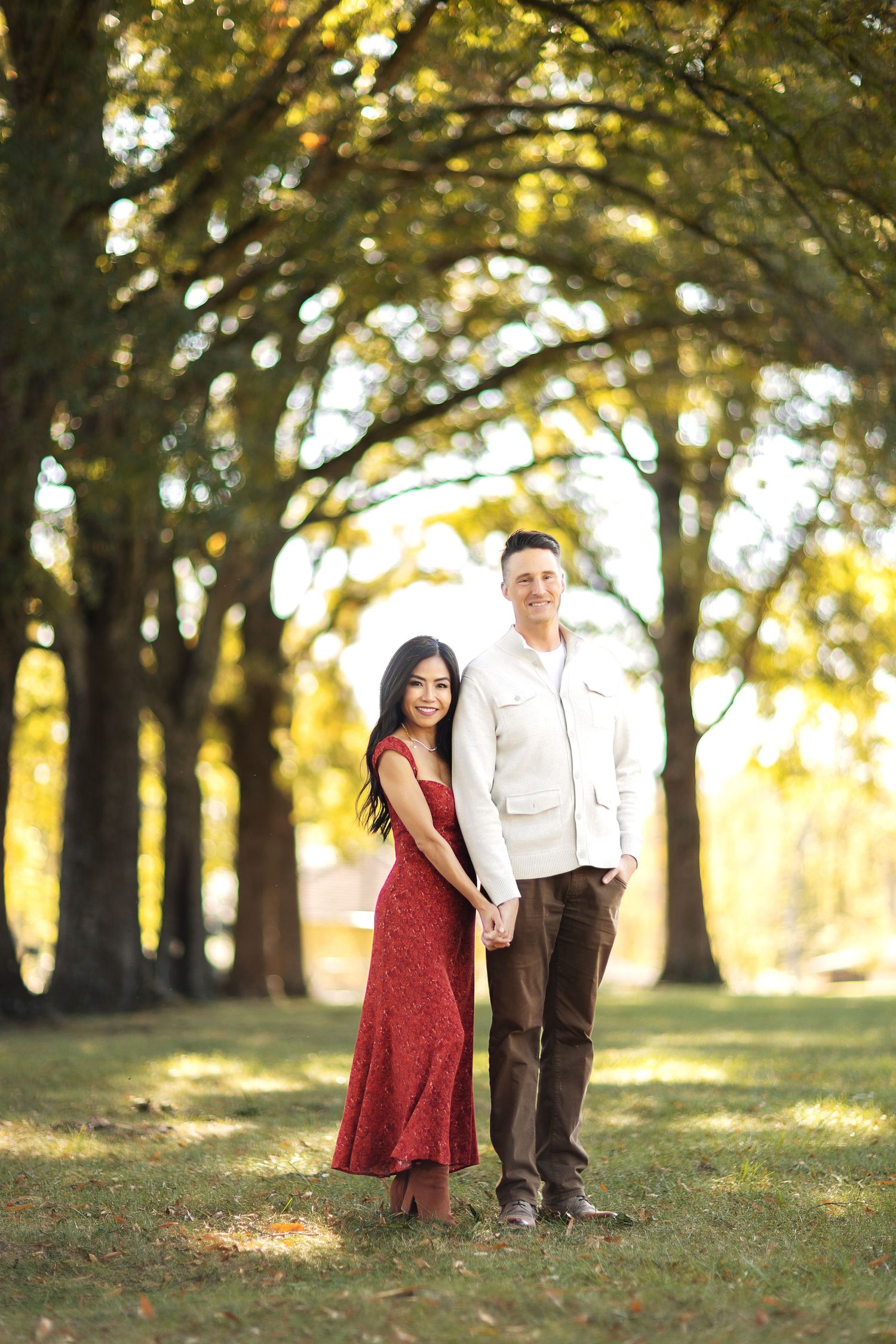 A couple poses together on an autumn day under a canopy of trees.