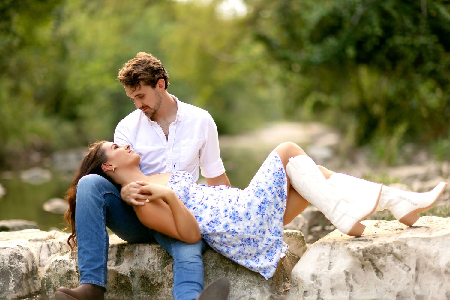 Romantic couple lounging on stone wall surrounded by greenery during outdoor photo session.