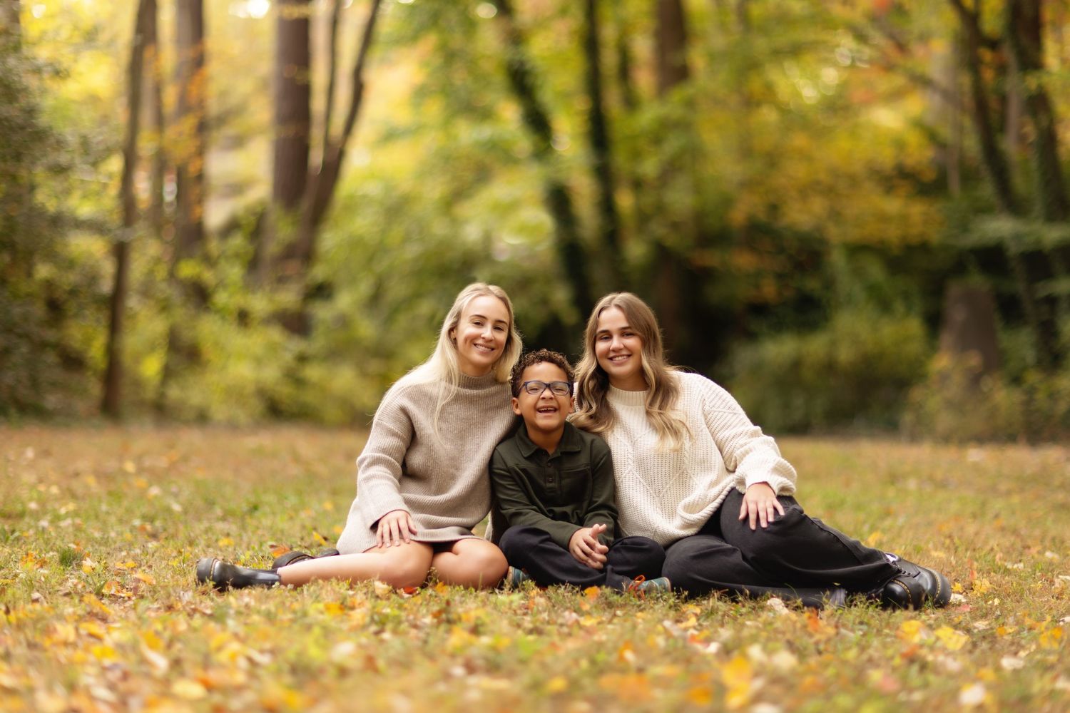 Family relaxing together on fallen autumn leaves in a wooded setting.