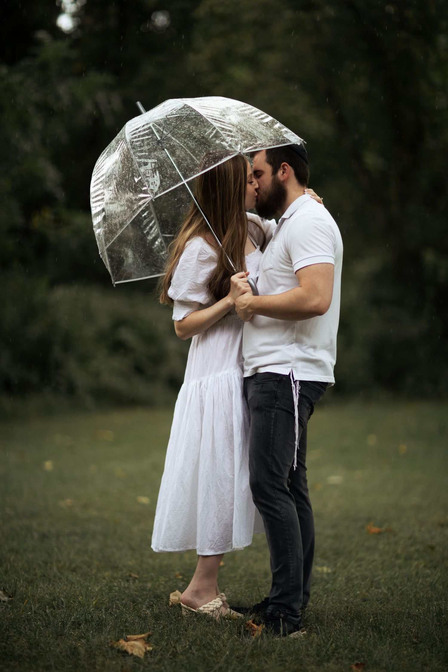 Romantic couple sharing moment under clear umbrellas in garden setting.
