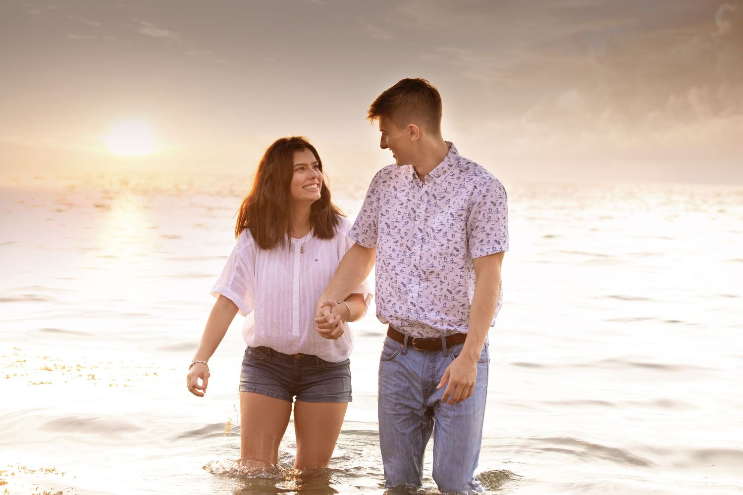 A couple walks along the beach during sunset for their engagement photos.