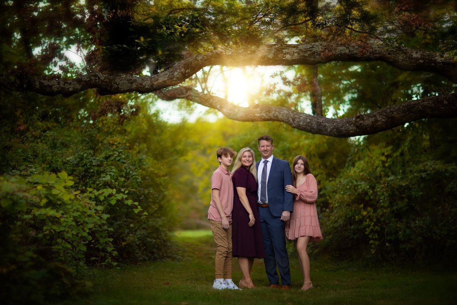 Family portrait session at sunset in a lush green park with golden sunlight filtering through the trees.