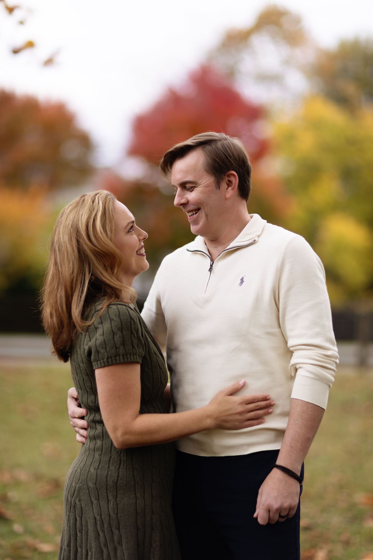 A couple laughs together during their autumn engagement photos with colorful fall foliage in the background.