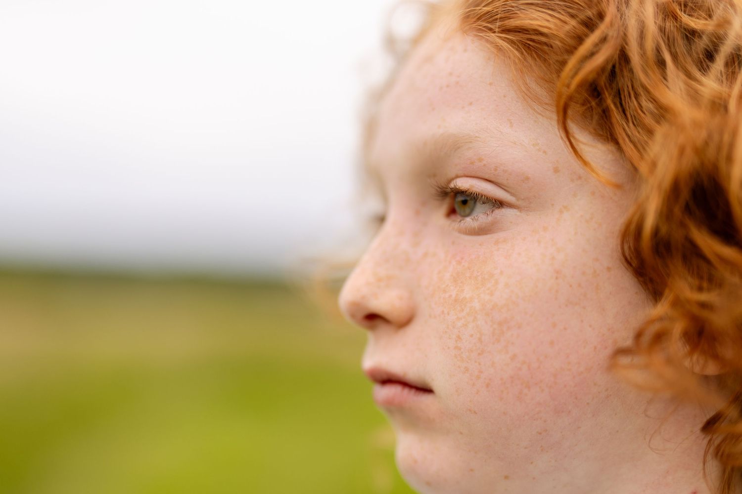 Close-up profile view of a young person with red hair against a blurred background.