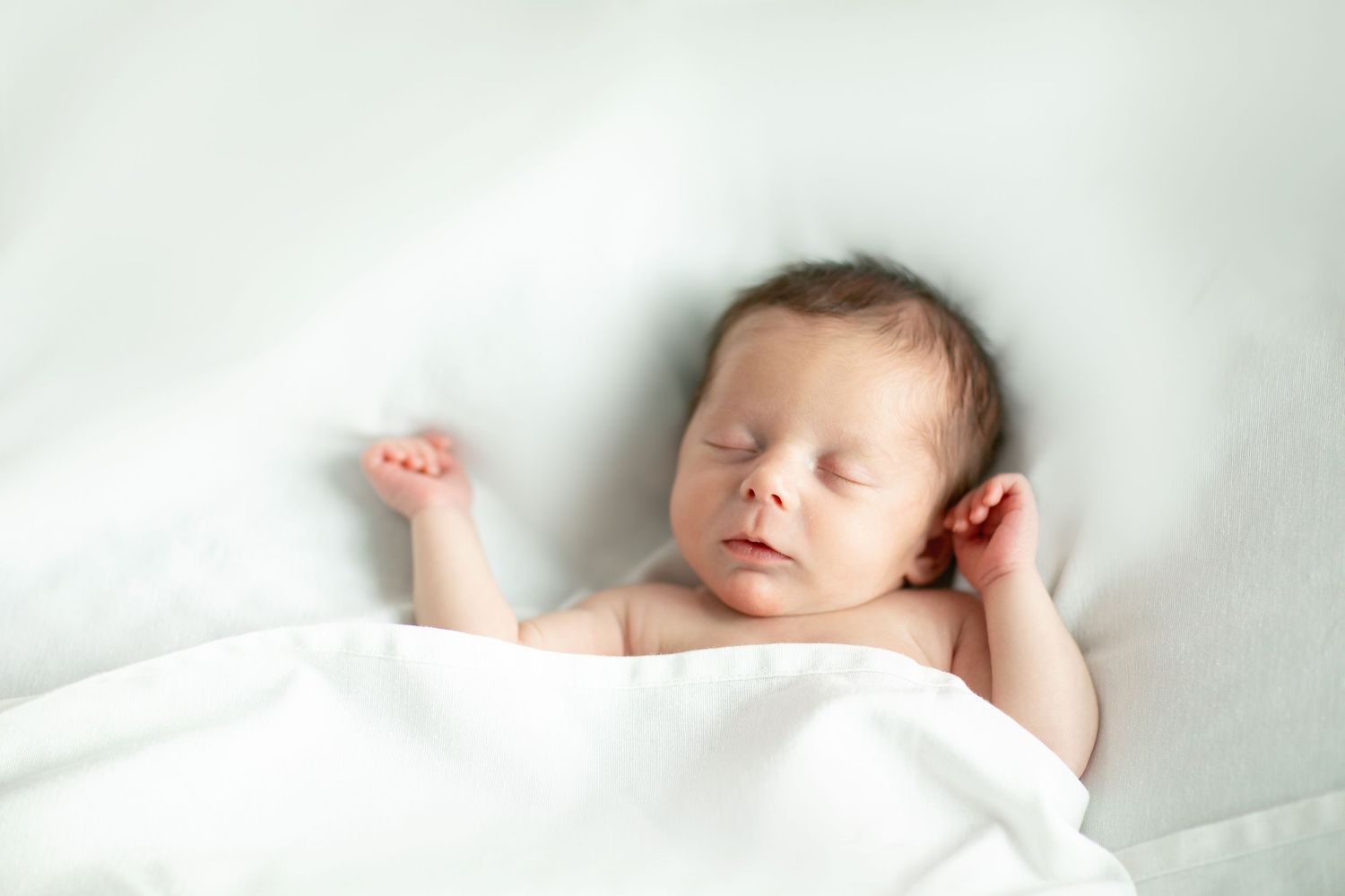 Sleeping newborn baby wrapped in soft white blankets on light background.