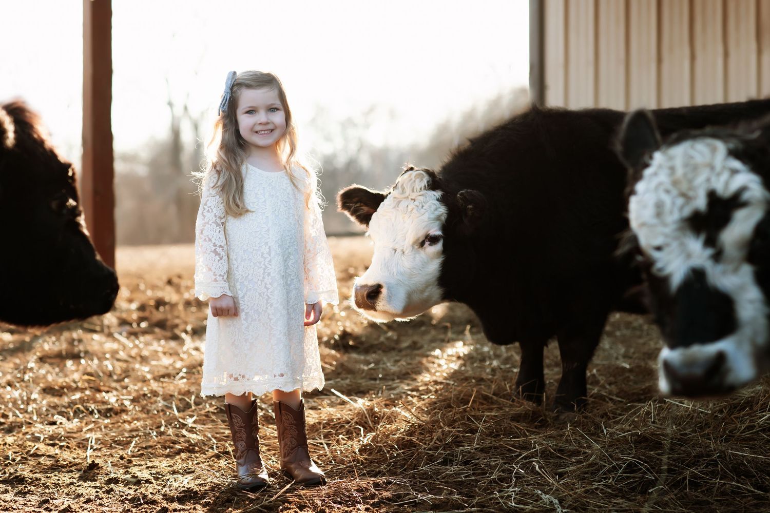Farm animals and children interact in a rustic barn setting with straw-covered ground.