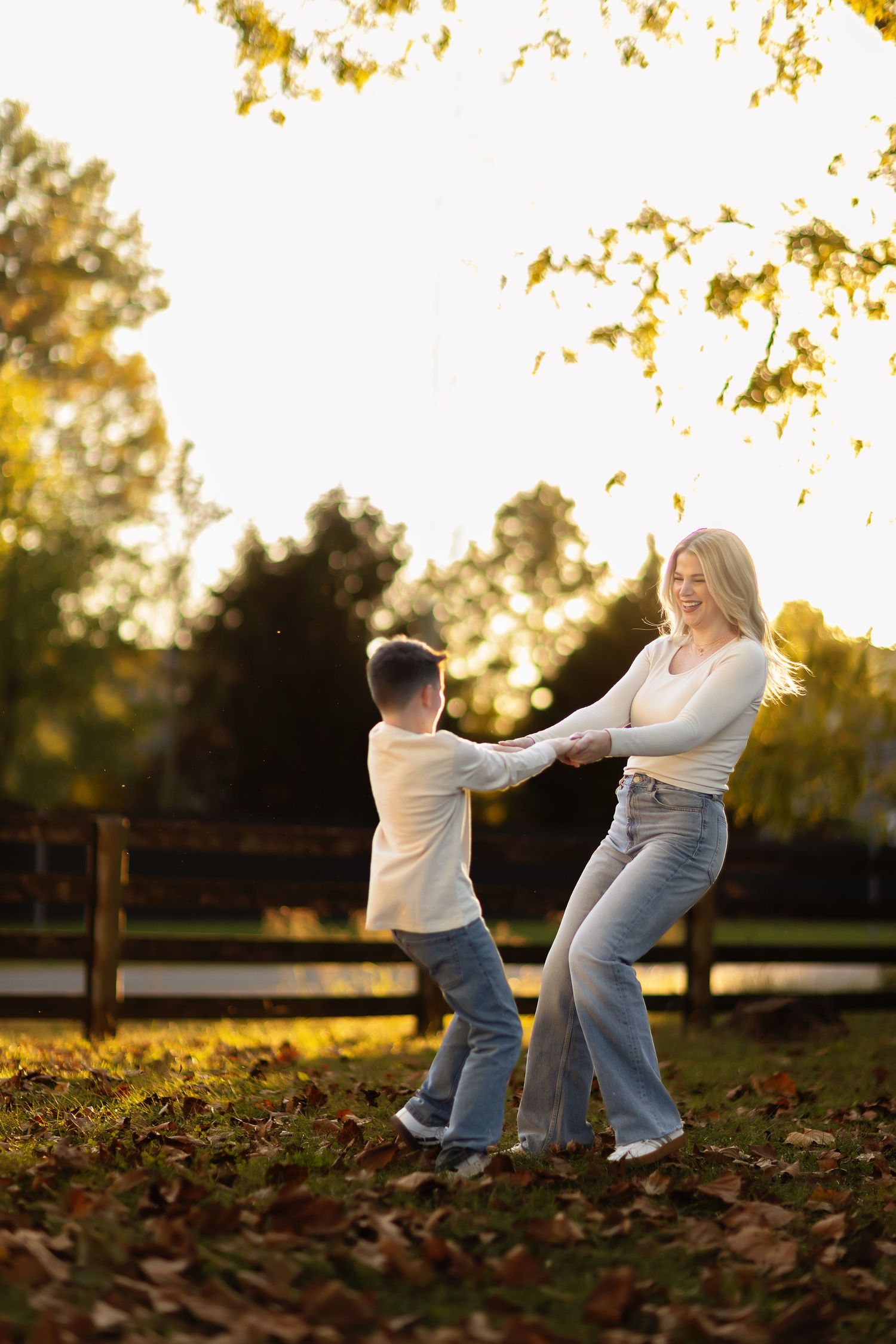 Playful moment between two people dancing in autumn leaves at sunset.