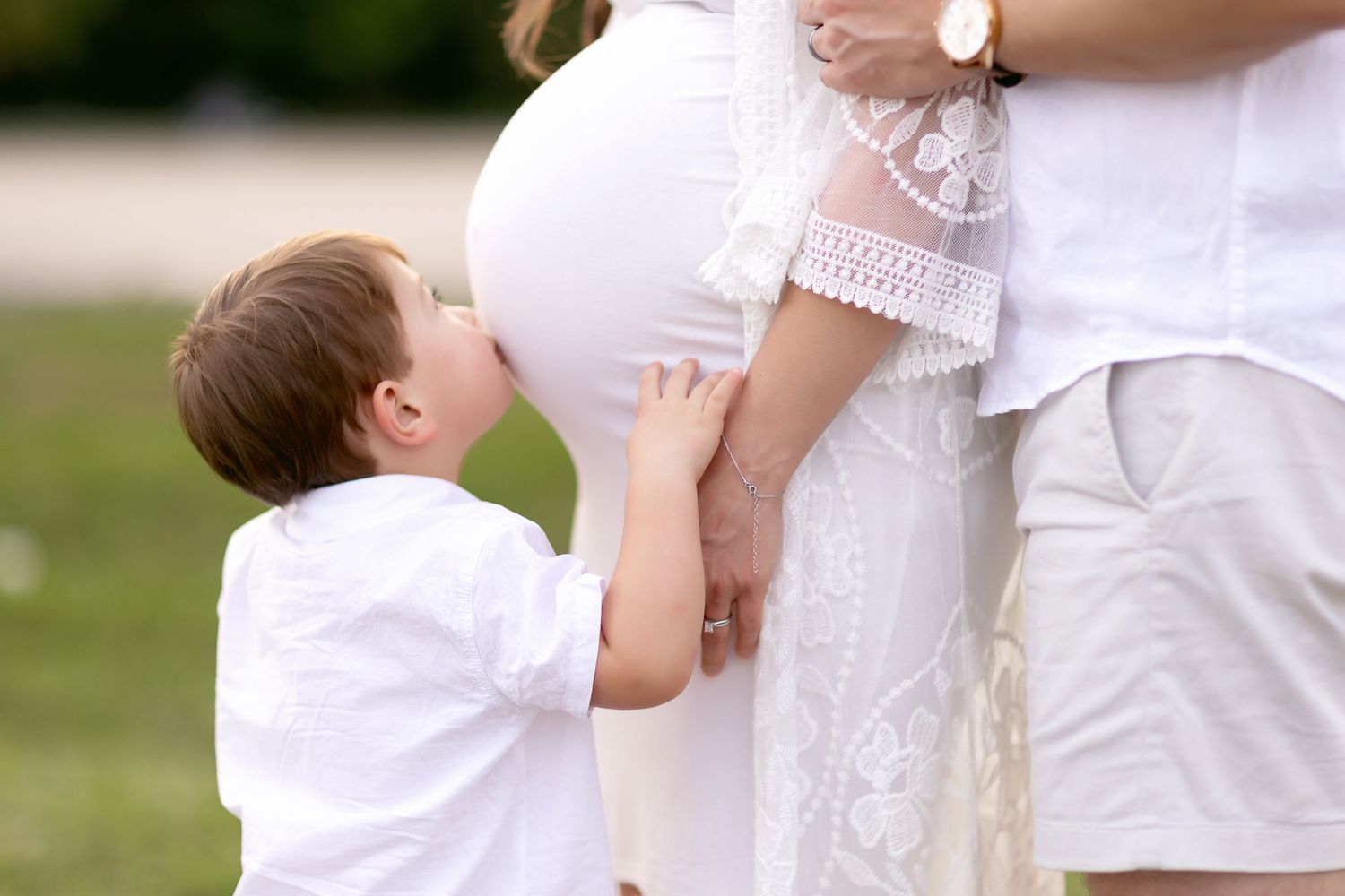Mother and child in white dresses share tender moment outdoors.