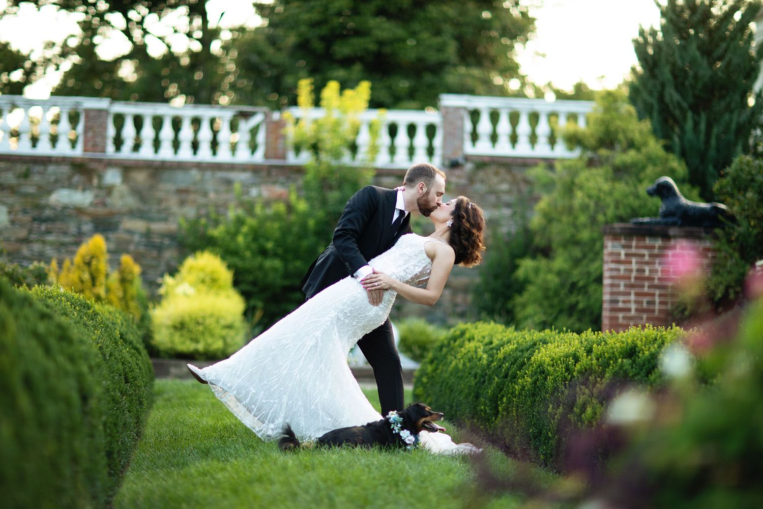 Couple in wedding attire dancing in elegant garden setting.