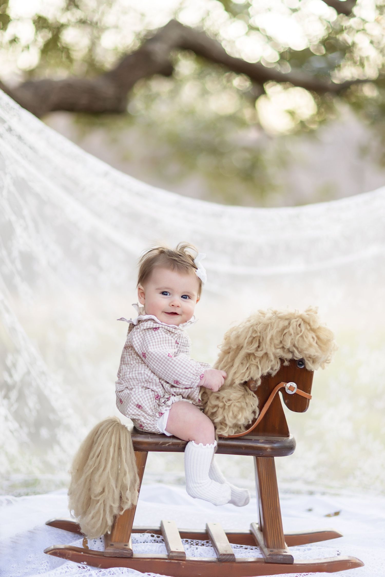 Wooden rocking horse toy with plush beige mane and saddle sits on white backdrop in outdoor setting.