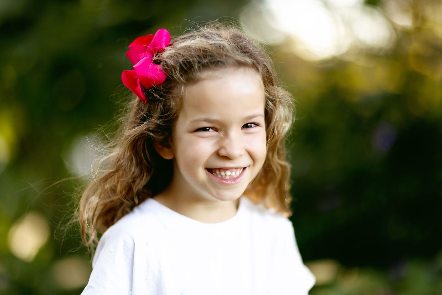 Young child wearing white shirt with pink flower in hair outdoors.