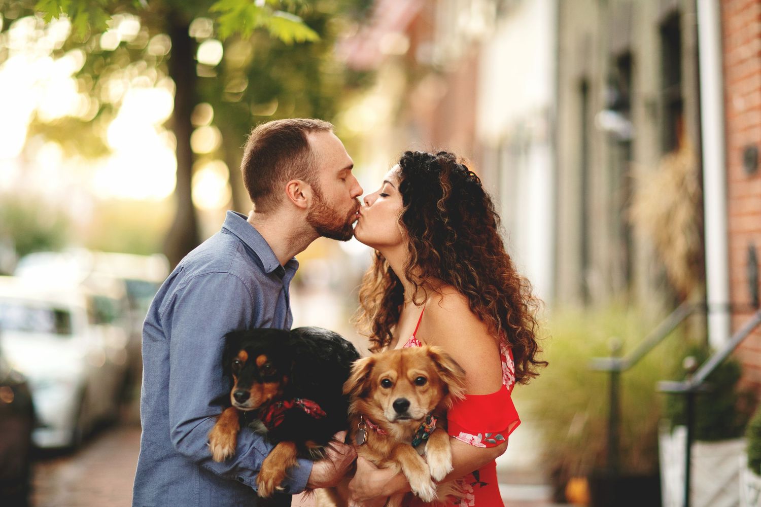 A couple shares a romantic moment with their dog on a sunny autumn street.