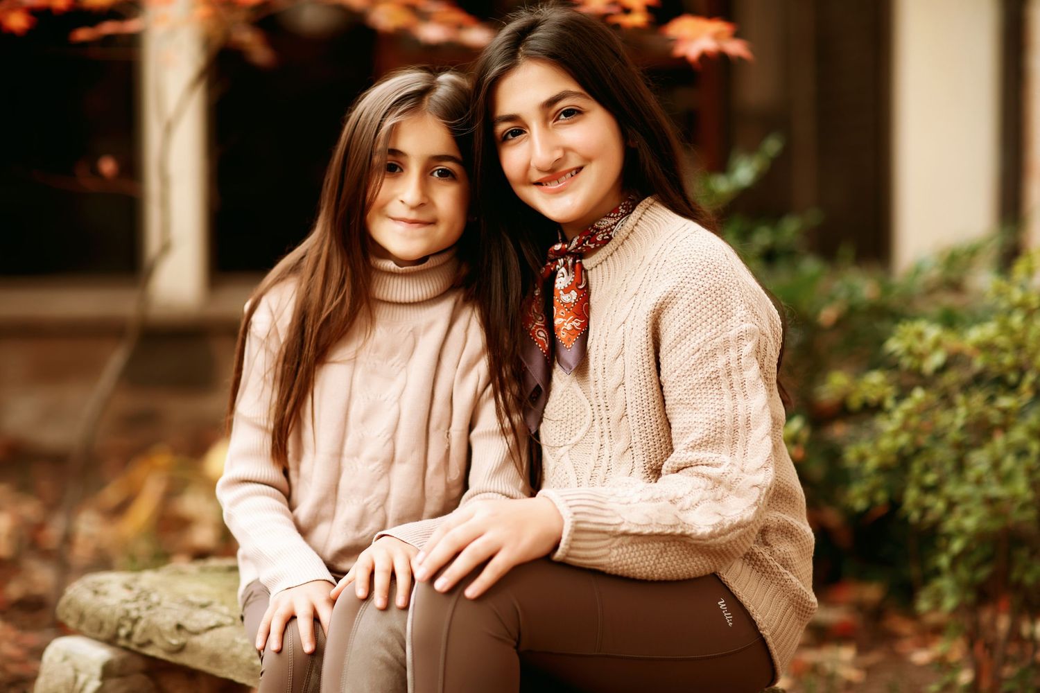 Two people in matching beige sweaters sitting close together outdoors.
