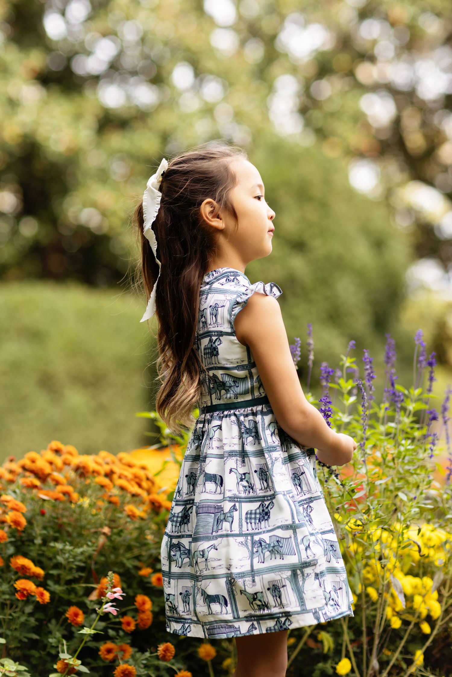 Young child in a patterned dress playing among colorful flowers in a garden.