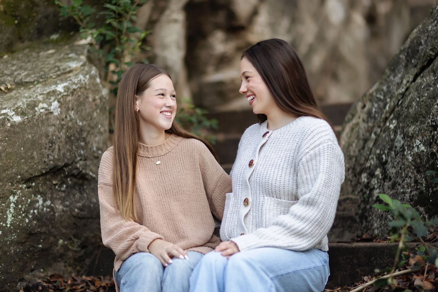 Two friends sharing laughter while sitting on rocks outdoors.