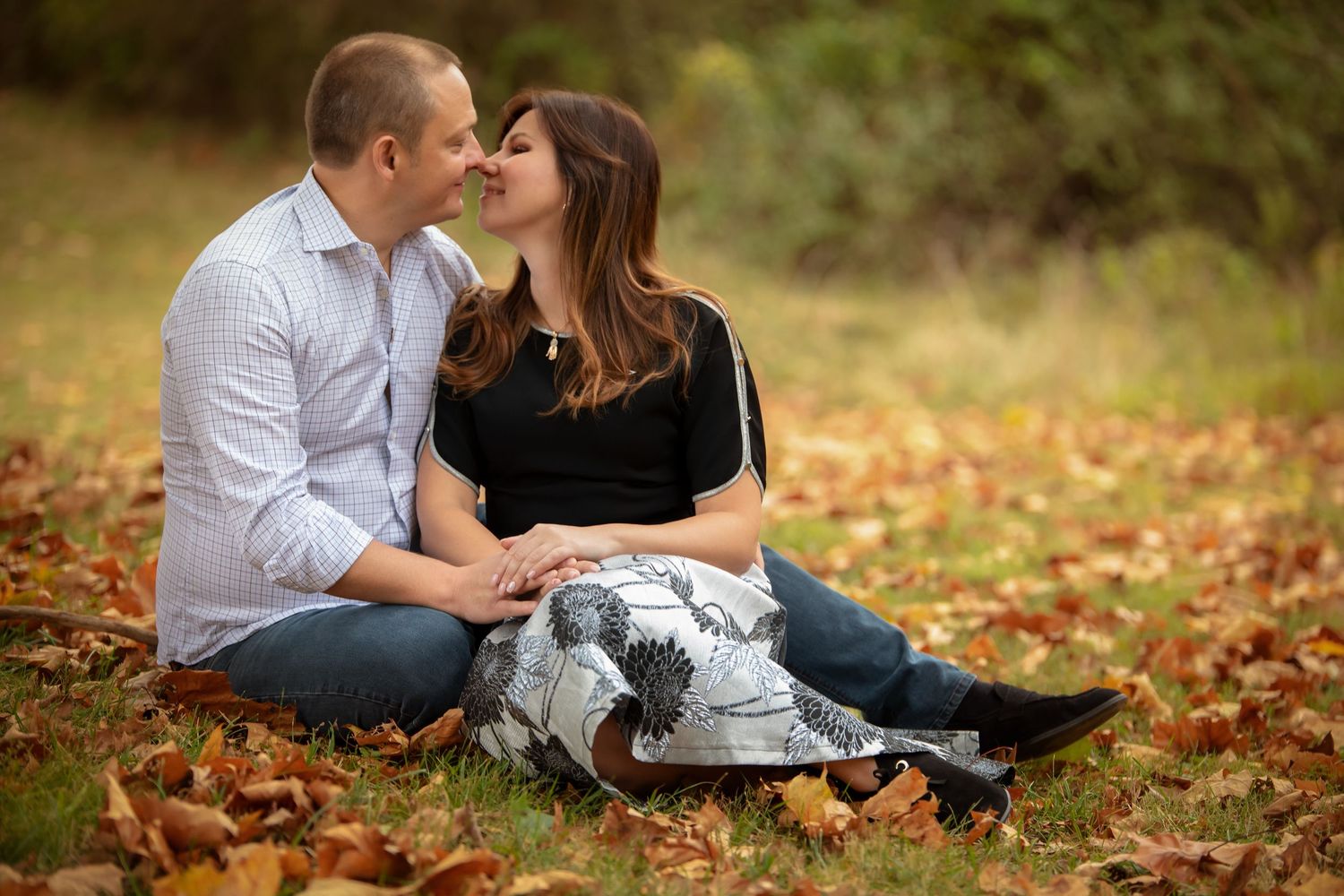 A couple sharing an intimate moment while sitting on autumn leaves.