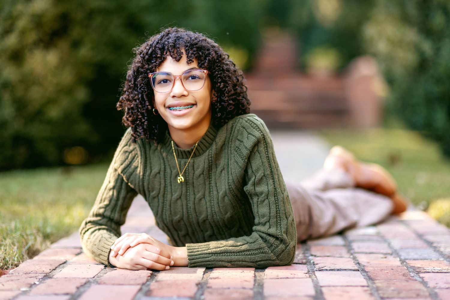 A person in an olive green sweater lies casually on a brick wall outdoors.