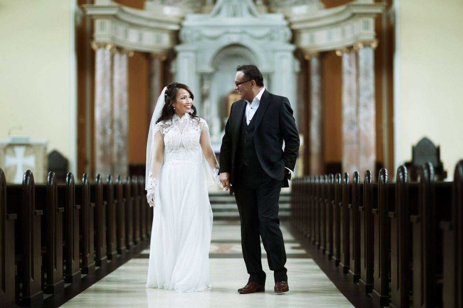 Elegant couple posing in a grand church aisle with ornate architecture.