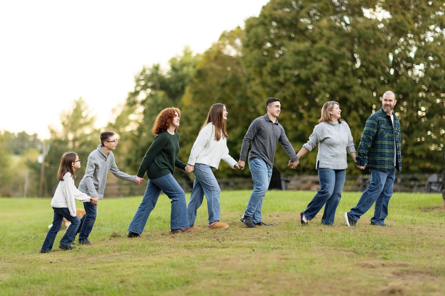 Group sitting in casual poses on grassy hillside during sunset photo session.