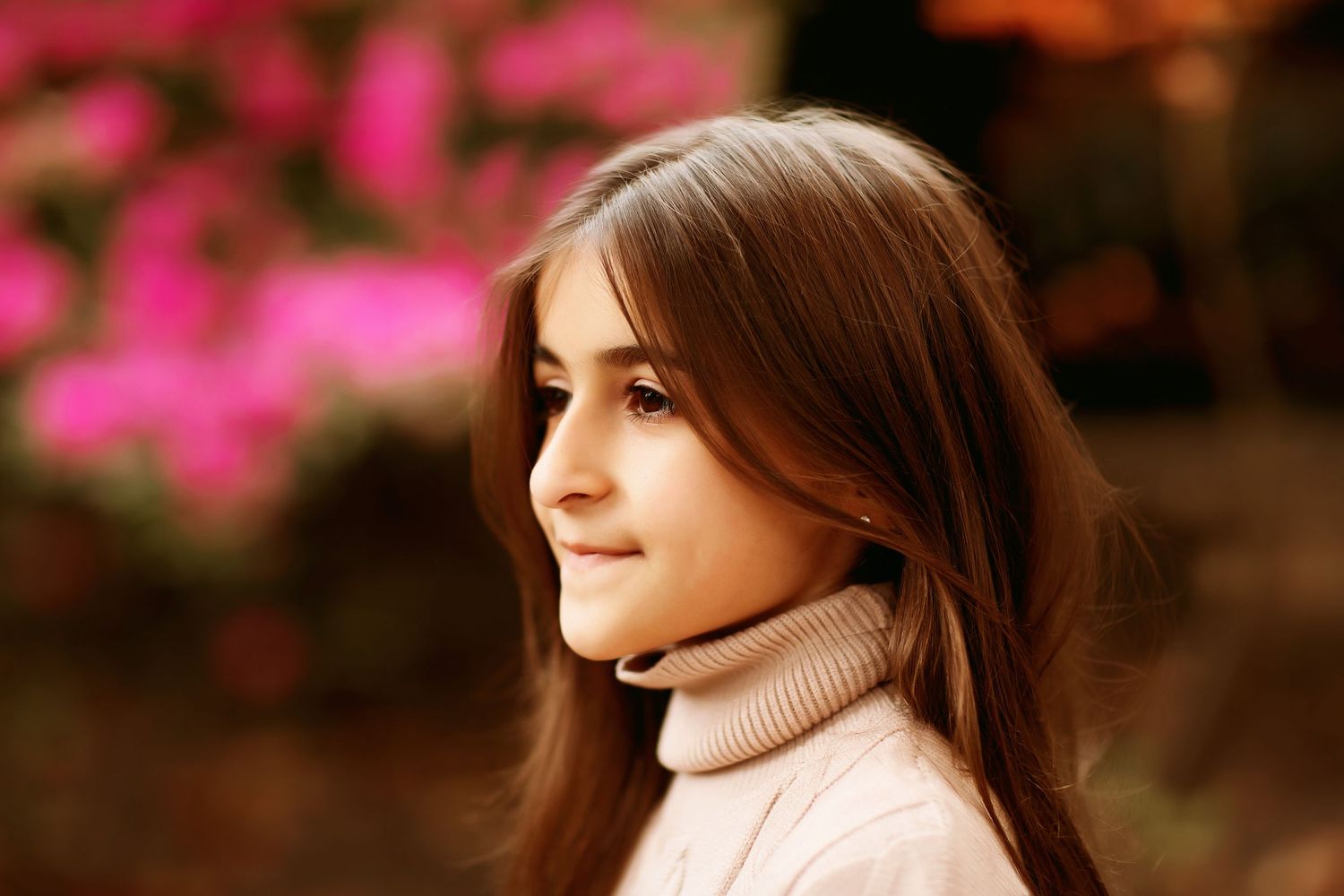 Portrait of someone in a turtleneck sweater with pink flowers in the background.