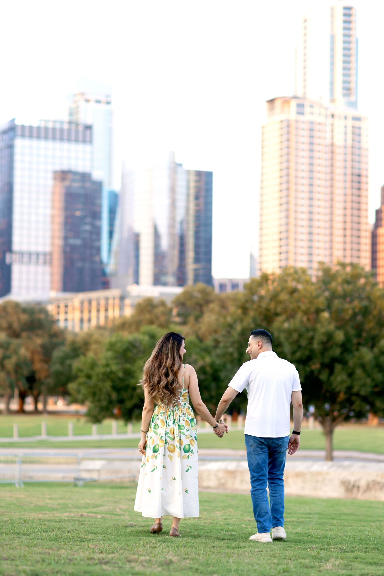 A couple walking hand in hand with city skyline in the background.