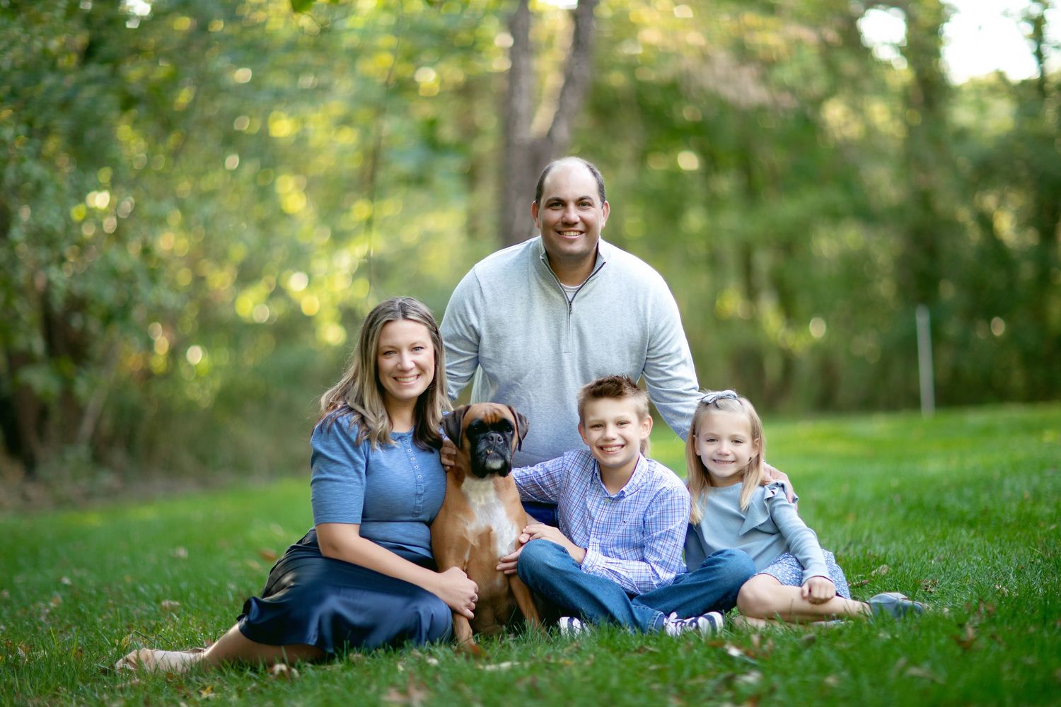 A family and their dog relax together on green grass during a summer photoshoot.