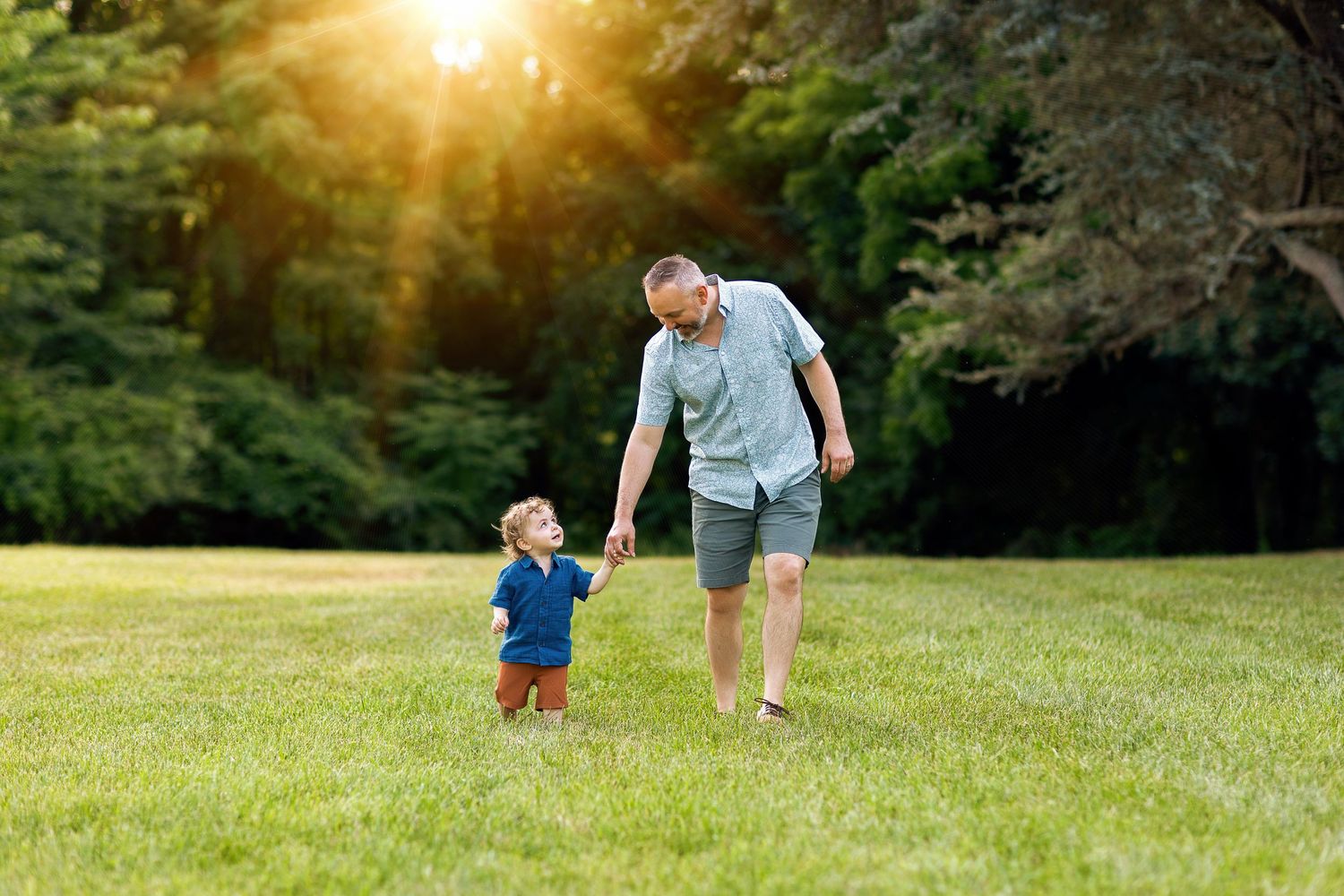 Parent and child walking together in grassy field during golden hour sunset.