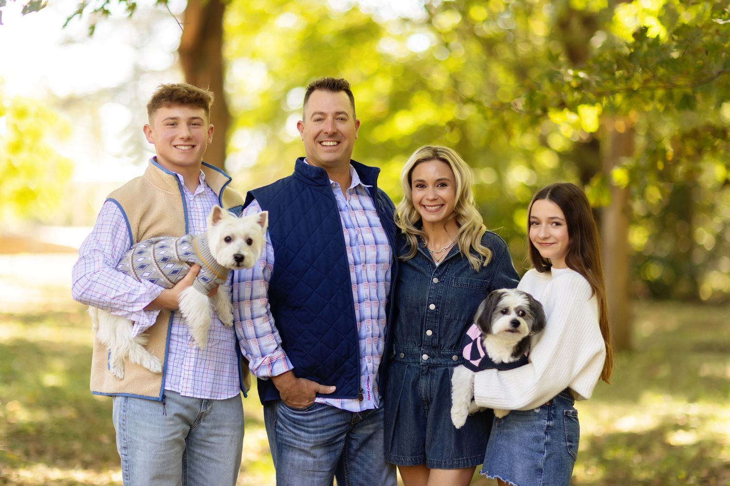 Happy family poses outdoors with their two adorable dogs in autumn sunlight.