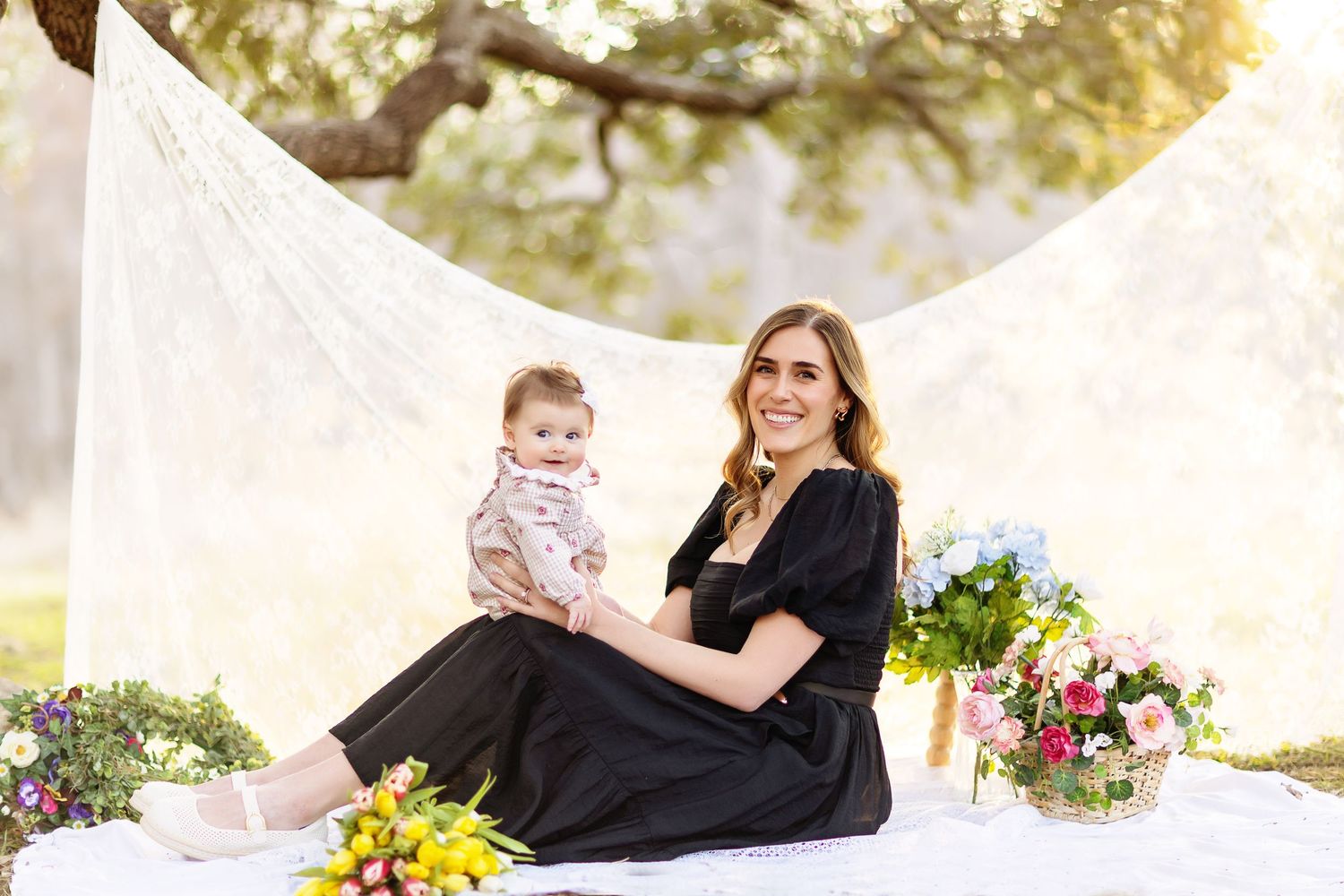 A group of people pose joyfully together outdoors with white fabric and colorful floral arrangements.