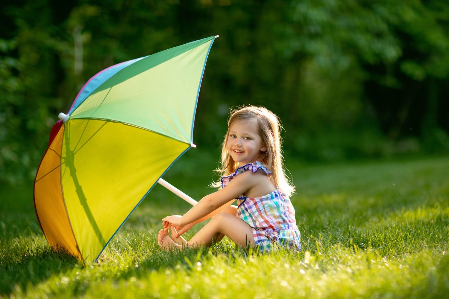 A colorful rainbow umbrella sits in lush green grass on a sunny day.