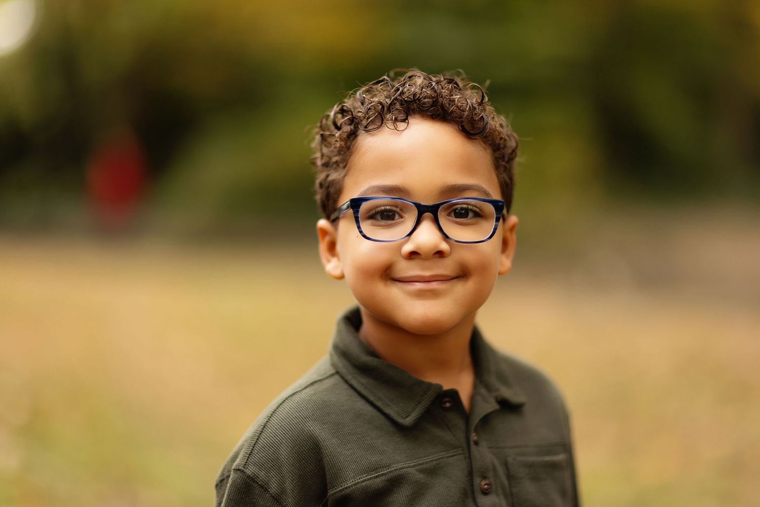 Child wearing glasses smiling outdoors in natural lighting.