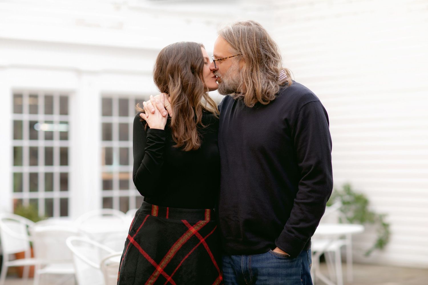 A couple shares an intimate moment in front of a white house during their photoshoot.