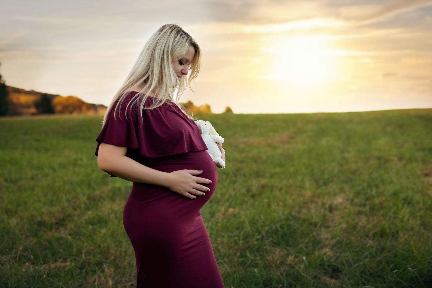 Maternity photos taken at golden hour in outdoor field setting.