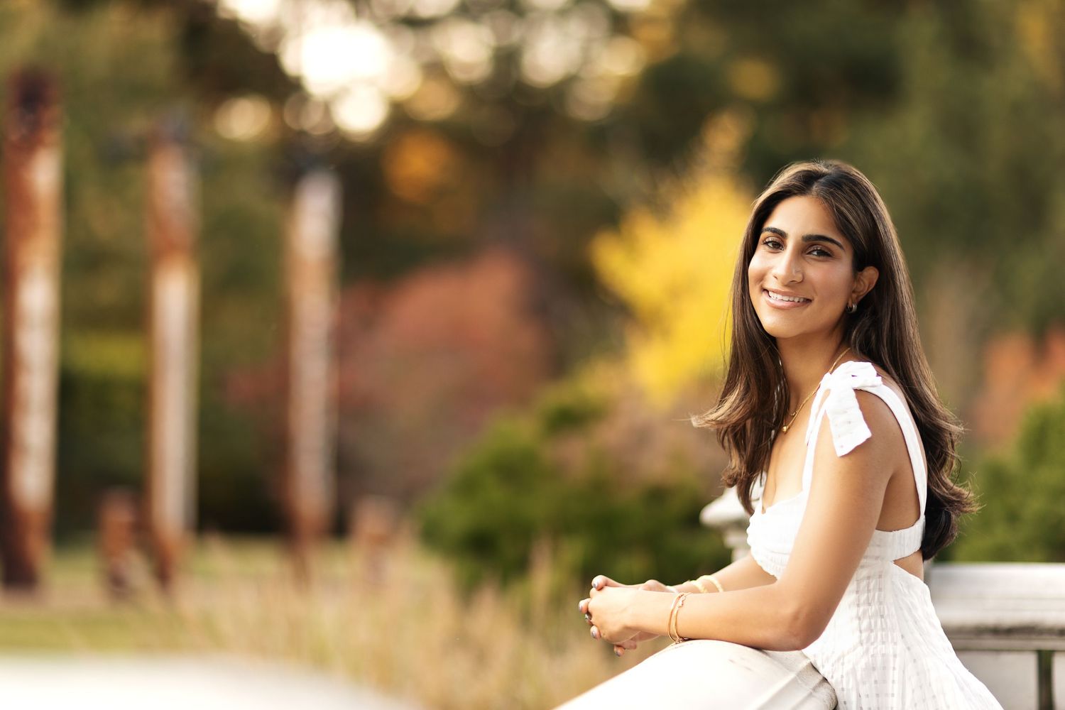 Woman in white lace dress poses outdoors during golden hour photography session.