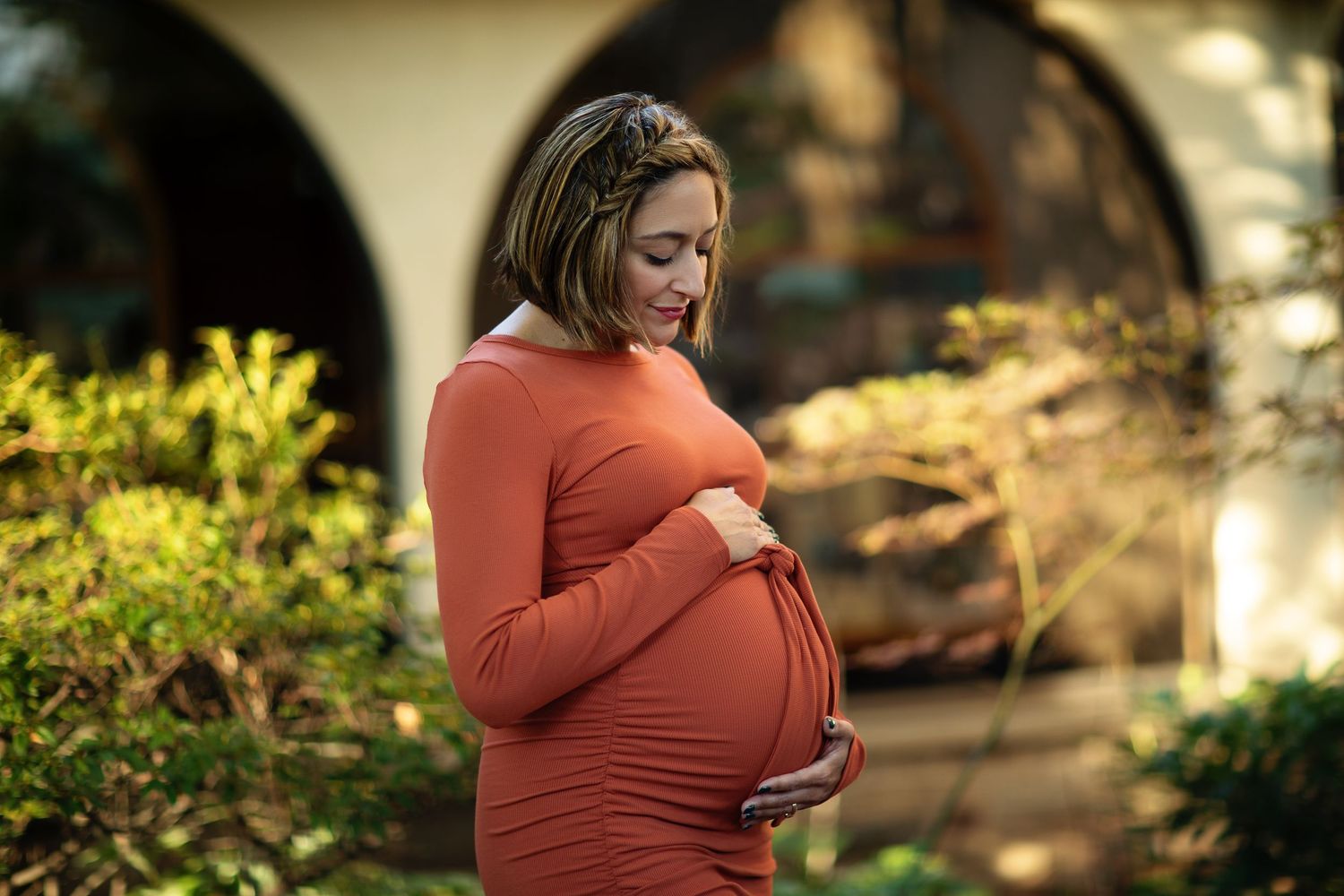 Warm sunlight filters through trees onto a rust-colored maternity photo session.