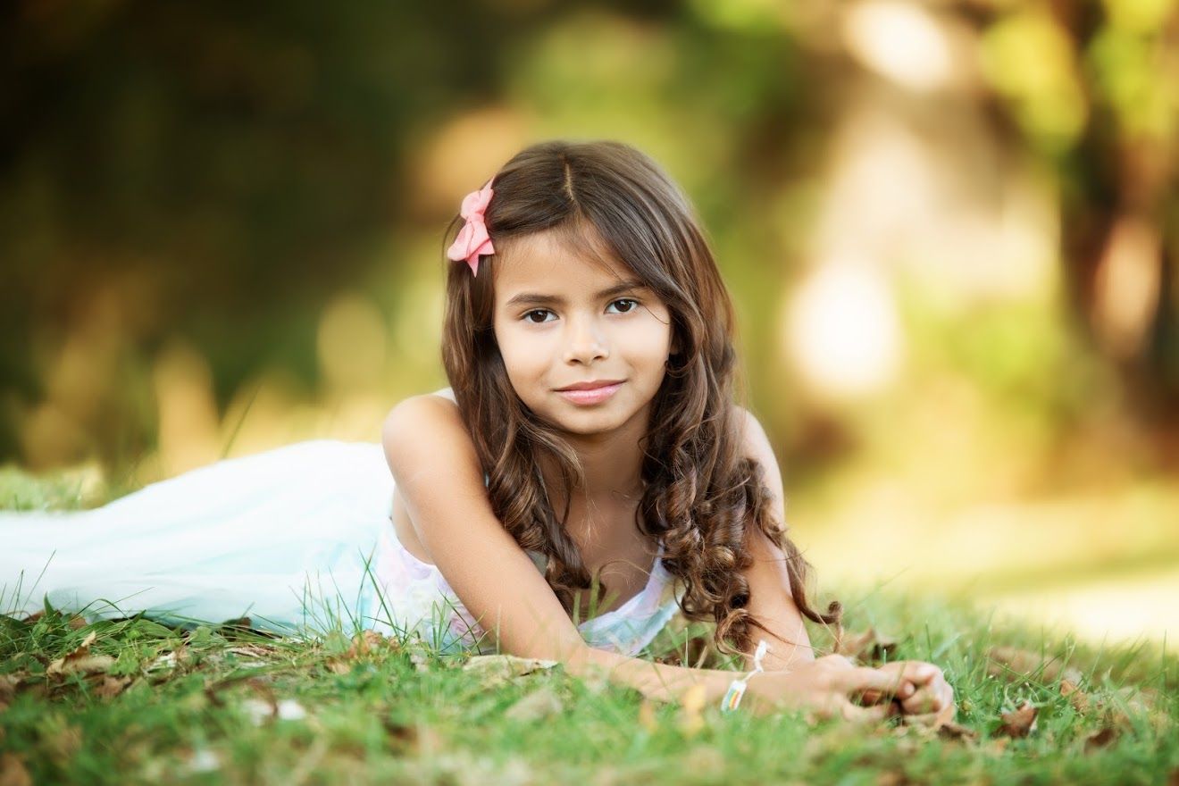 A child lies in green grass during a warm summer day with golden sunlight filtering through.