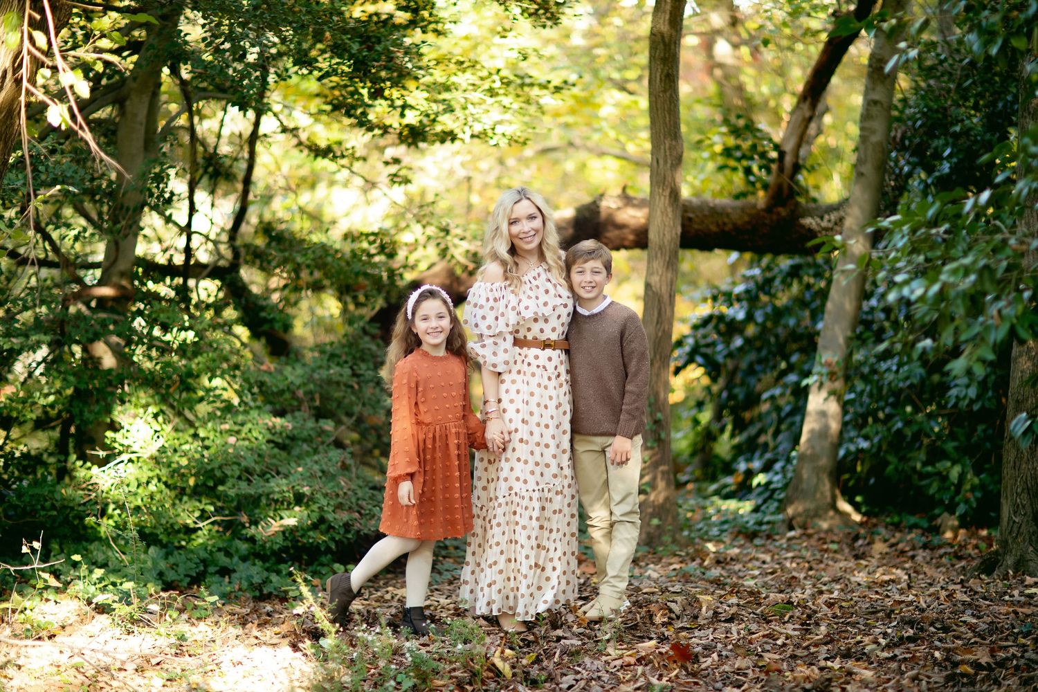 People walk through a lush wooded path during a sunny autumn day.