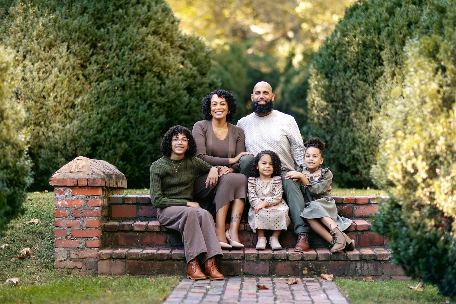 A family relaxes together on a brick wall bench in a scenic outdoor garden setting.