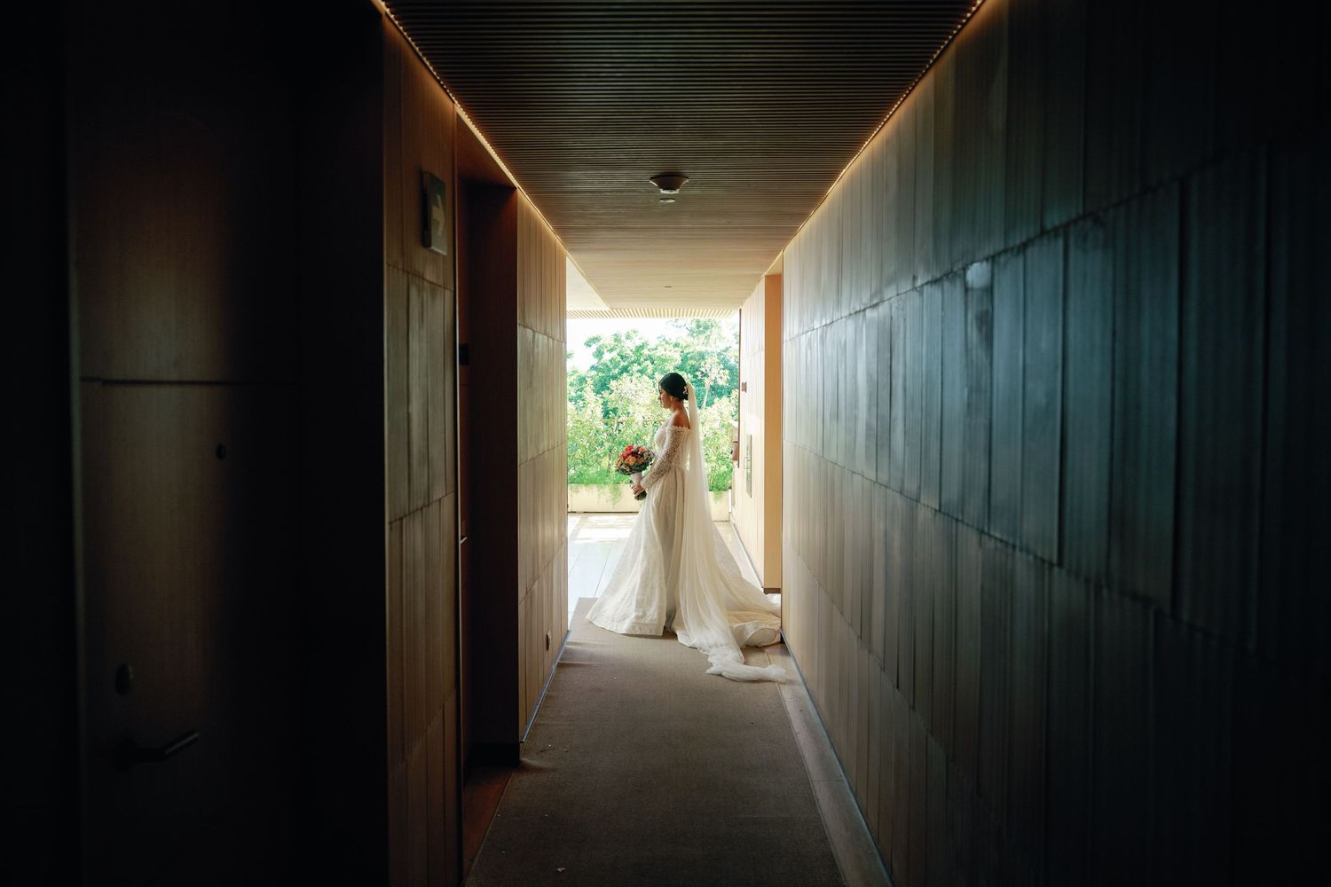 Dark hallway with wooden paneled walls leads to a bright window at the end creating a dramatic light tunnel effect.