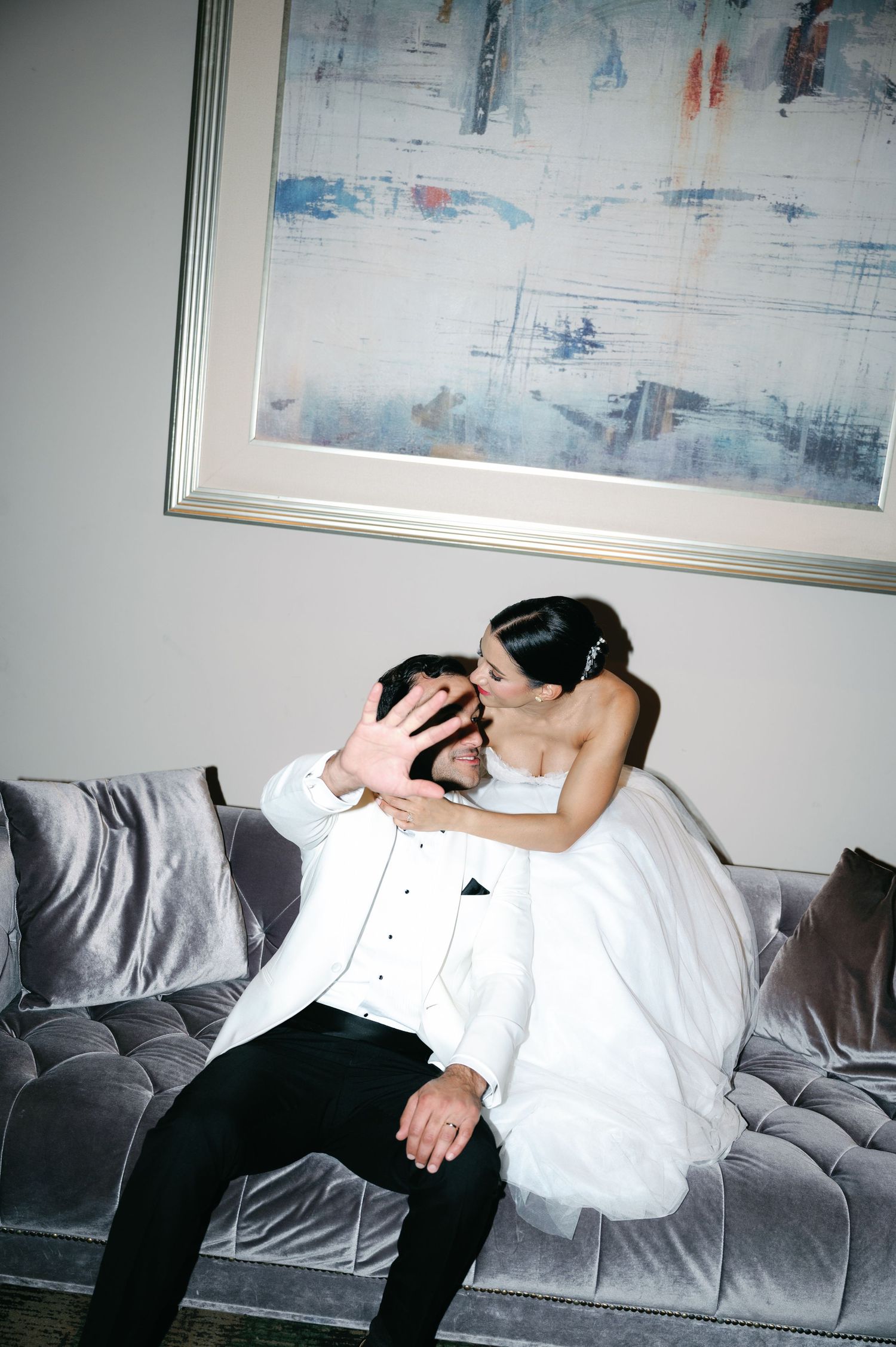 A person in white and black attire rests on a gray couch beneath abstract artwork on the wall.