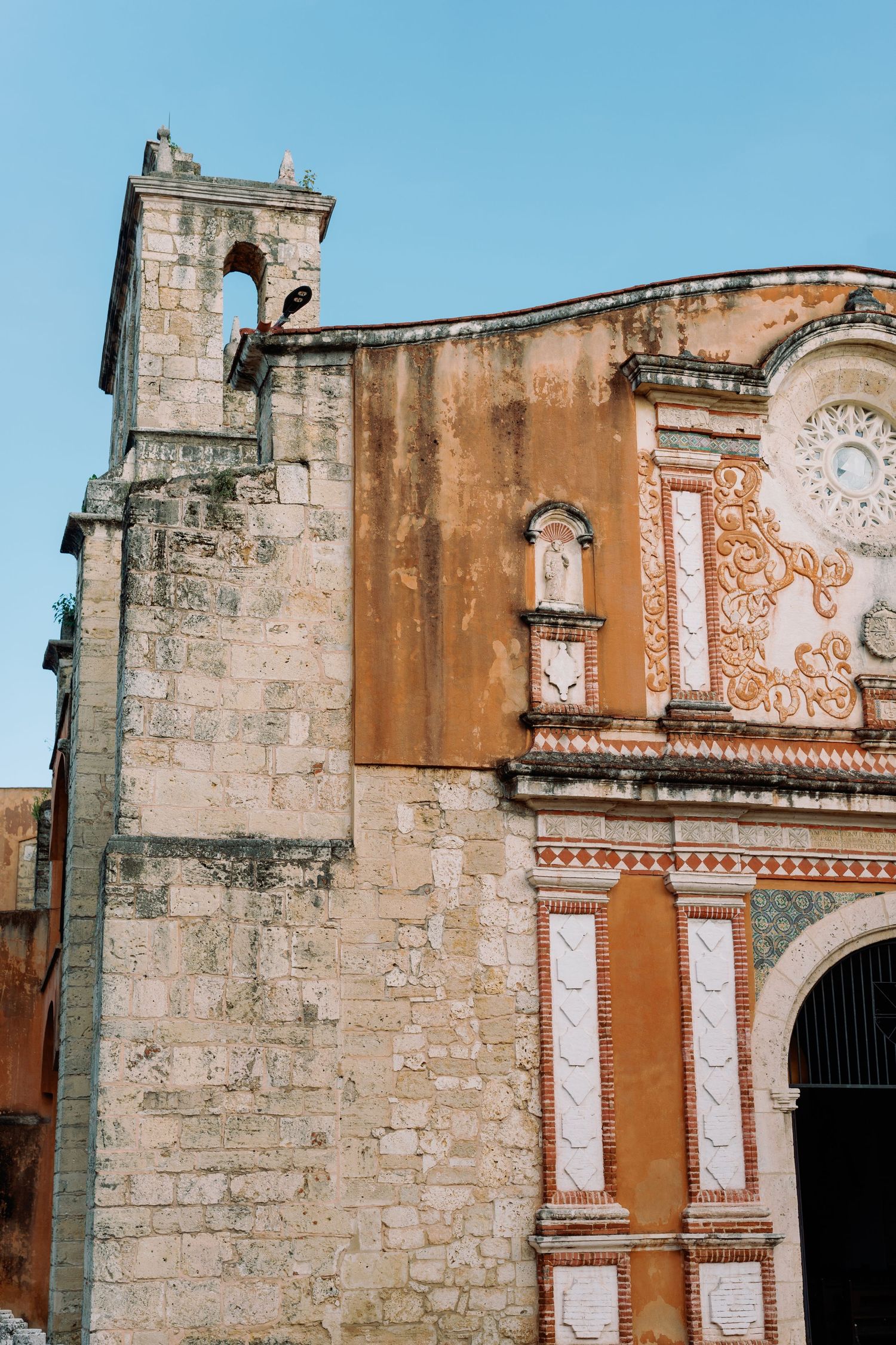 Architectural details of an old Spanish colonial church facade with terracotta walls and white stone decorative elements.