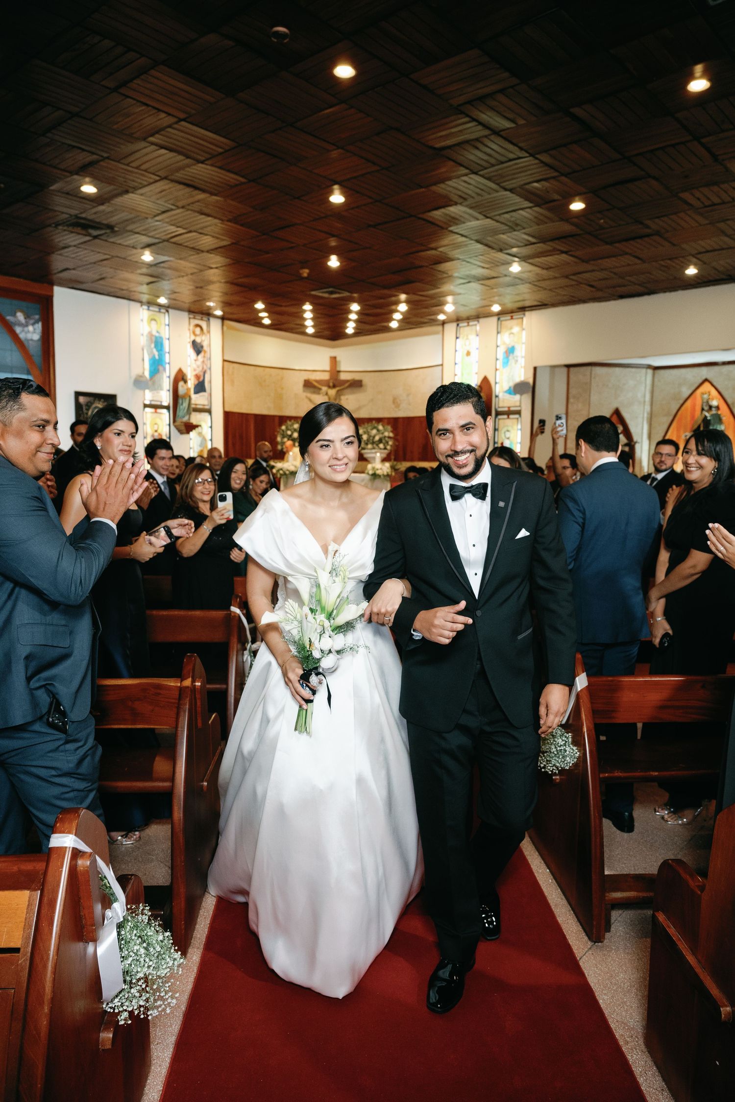 Wedding party walks down church aisle after ceremony with guests celebrating on both sides.