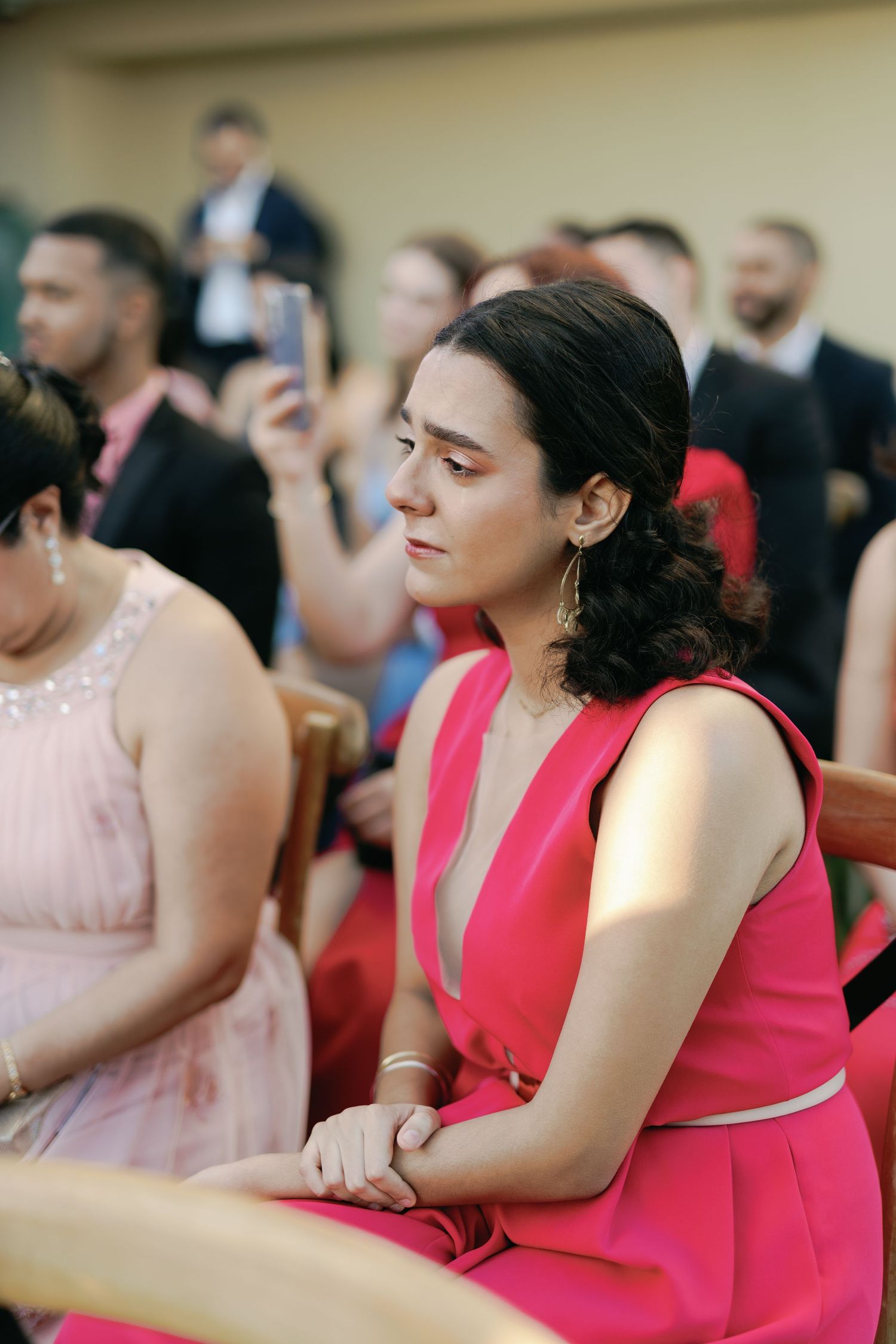 Wedding guests seated in formal attire watch attentively during an indoor ceremony.