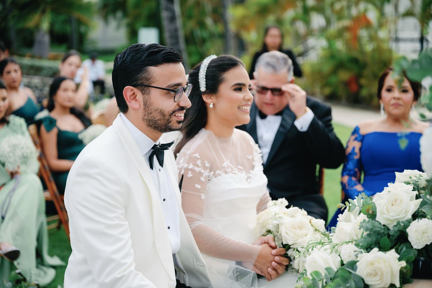 Wedding guests and wedding party gathered on a lush tropical lawn during an outdoor ceremony.